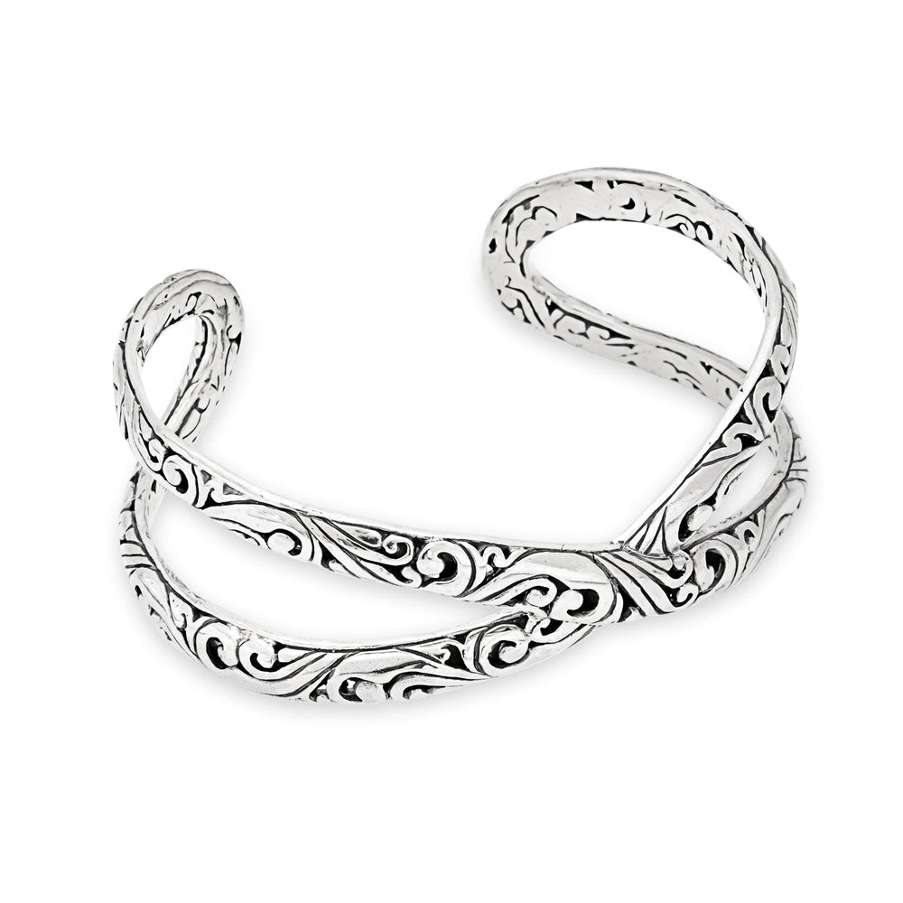 A silver bangle bracelet with an intricate crossover design, featuring a high polish finish with oxidised detail.