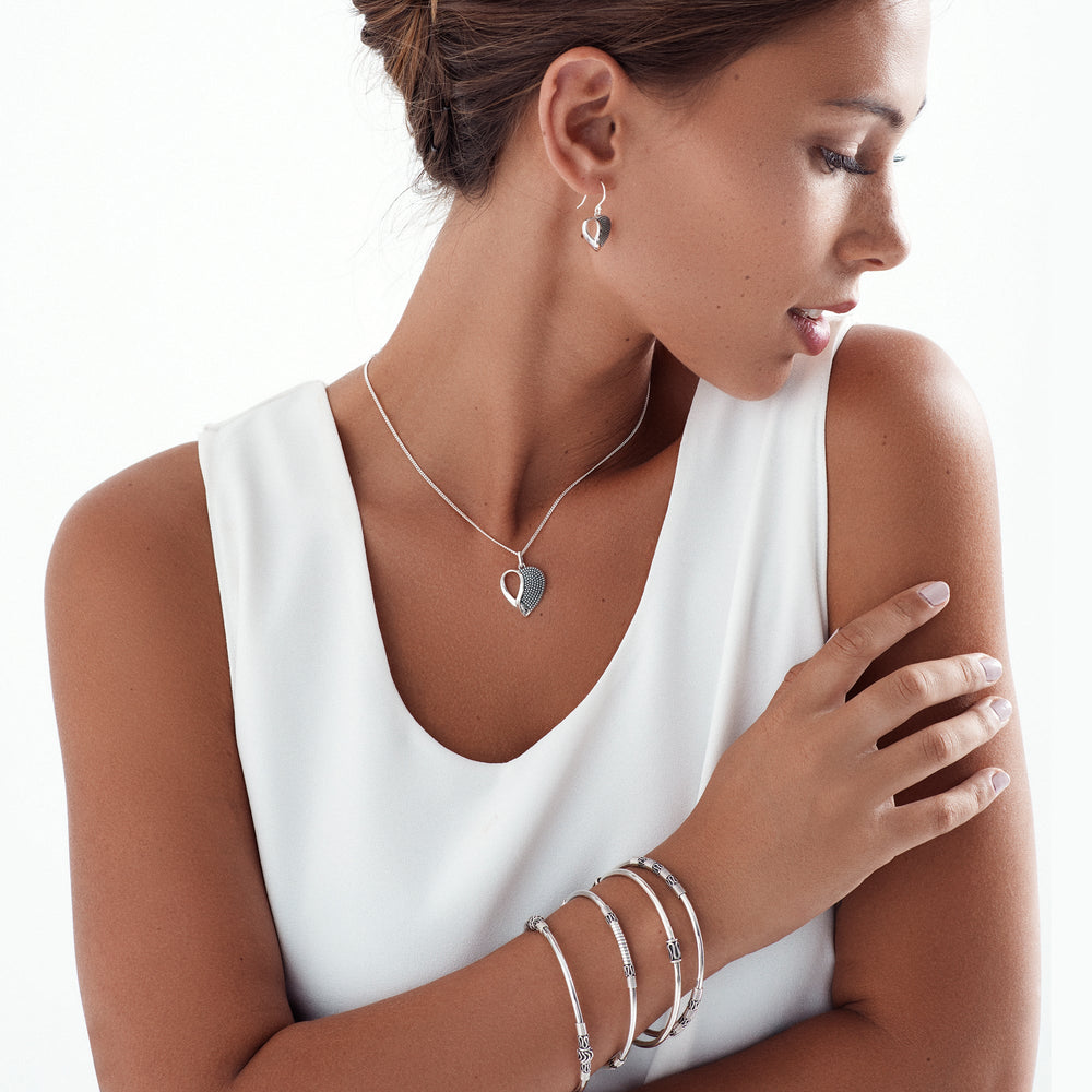 A 925 sterling silver bangle with a high polish finish and oxidised detail, featuring a unique design on female model.