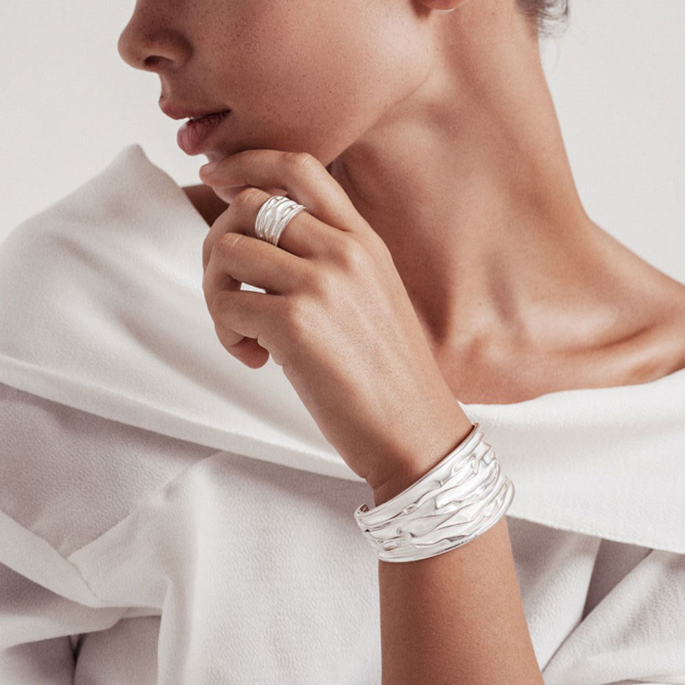 A sterling silver ring with a band design that resembles ocean waves, with a high shine finish and satin depths and silver waves bangle. 