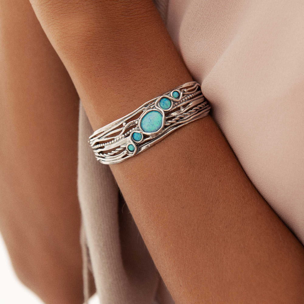 A silver bangle bracelet with blue opal stones set in an openwork design, displayed on a woman model