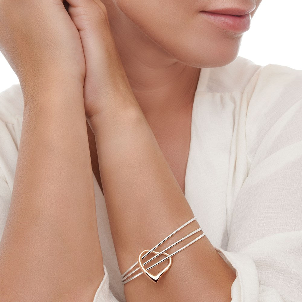 Three silver bangles with a rose gold heart connector on a female model