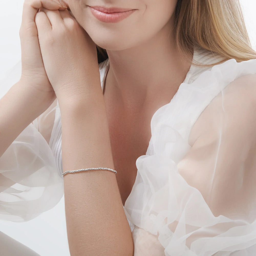 A bracelet made of mini silver pebble beads with a high polish finish, featuring a high polish finish and a small circular charm at the end.