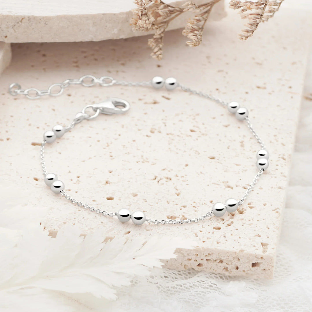 A silver bracelet with twin beads on a classic link chain, displayed on a white surface with a patterned background.