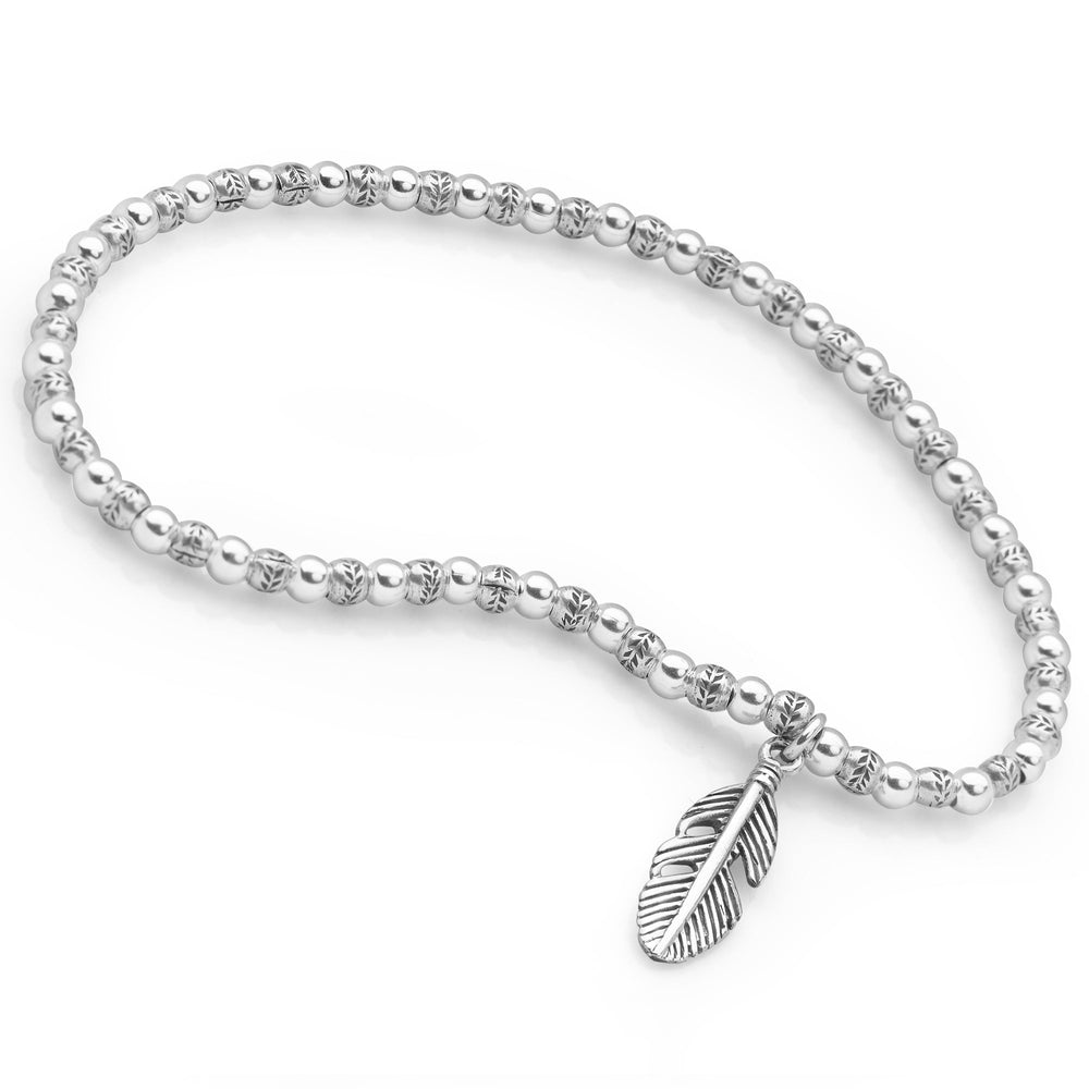 A silver bracelet with small beads and a silver feather charm, designed for stacking on white background