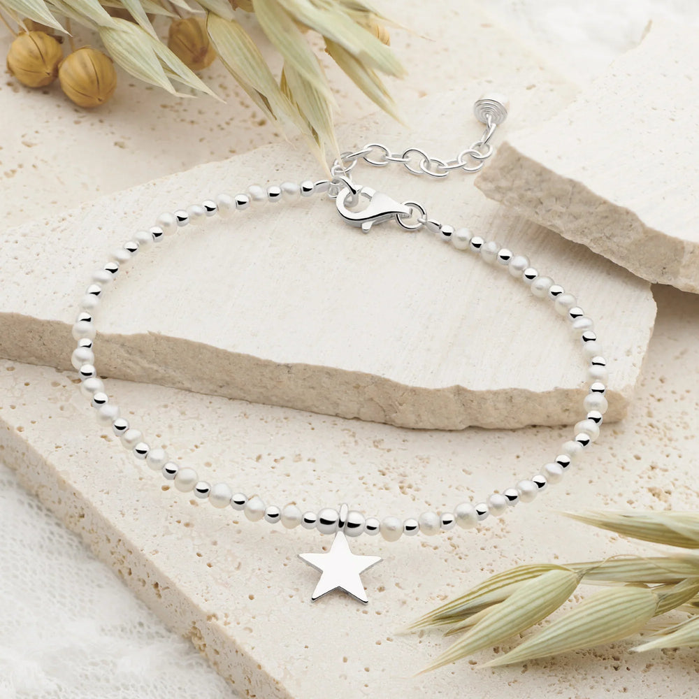 Silver bracelet with a star charm on a natural stone surface with dried plants.