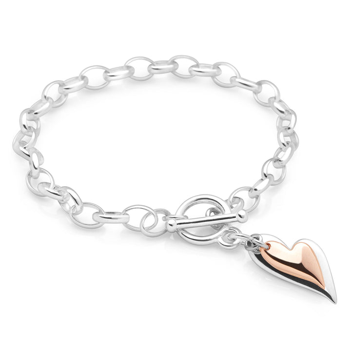 A silver bracelet with a rose gold-plated heart charm, featuring a T-bar fastening on a chain on white background