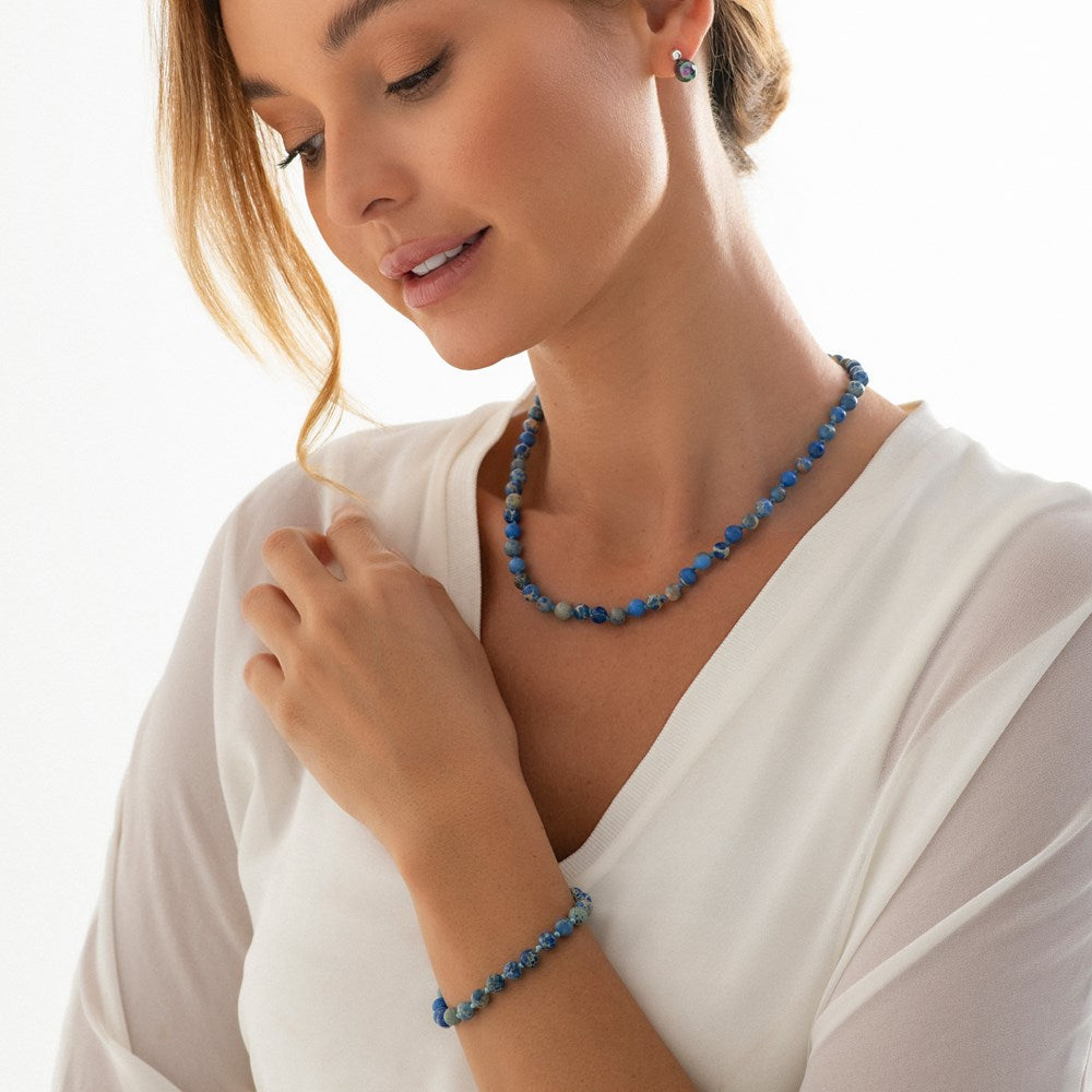 A bracelet with smooth blue variscite beads and a silver star charm, displayed on a white textile surface with floral accents on model