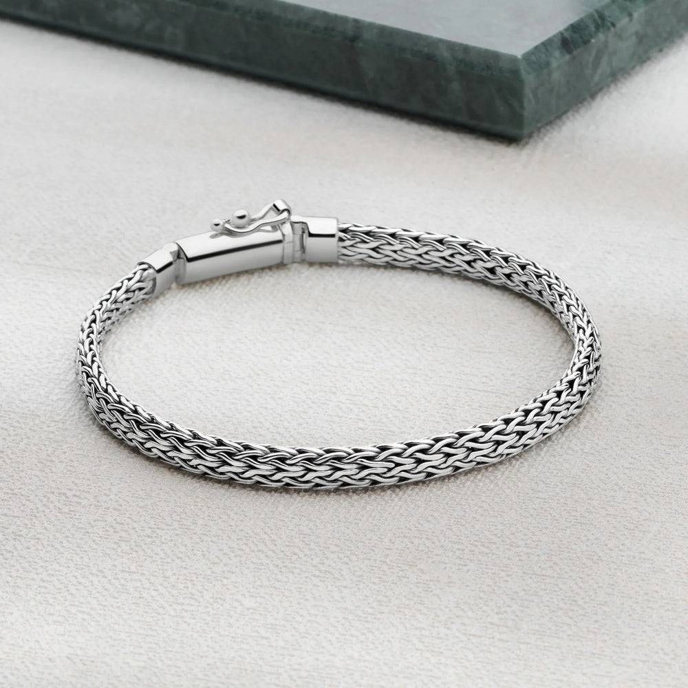 Silver braided bracelet on a light gray surface with a green marble block in the background