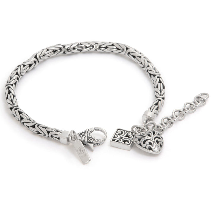 Silver bracelet with braided design and heart-shaped charm on a white background