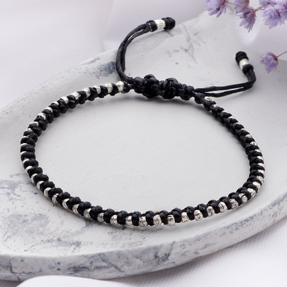 An interwoven bracelet featuring black cord and 925 sterling silver beads, displayed on a marble surface.