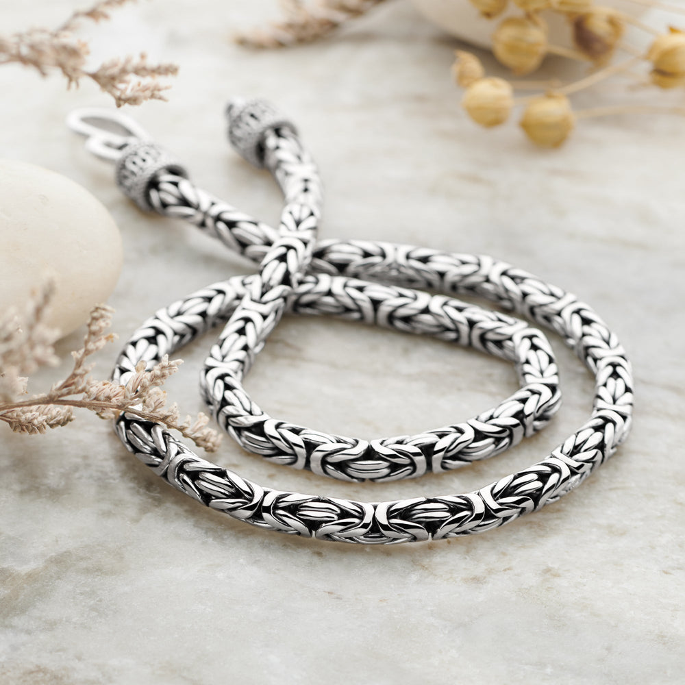 A silver Byzantine Balinese chain necklace with a polished finish, displayed on a marble surface.