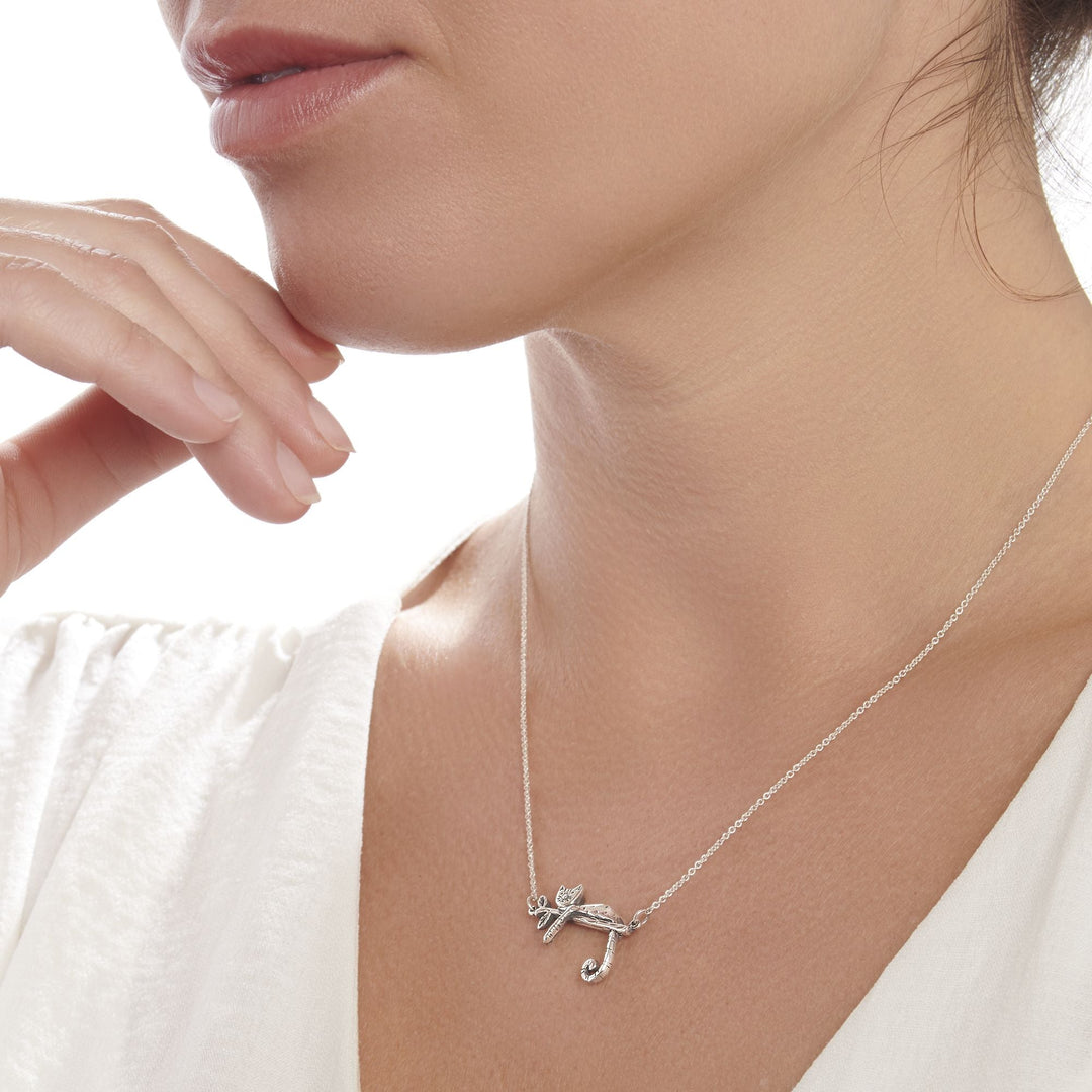 A silver necklace with a pendant in the shape of a relaxed kitty-cat, lying on a branch.