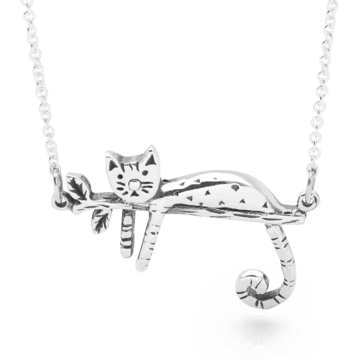 A silver necklace with a pendant in the shape of a relaxed kitty-cat, lying on a branch.