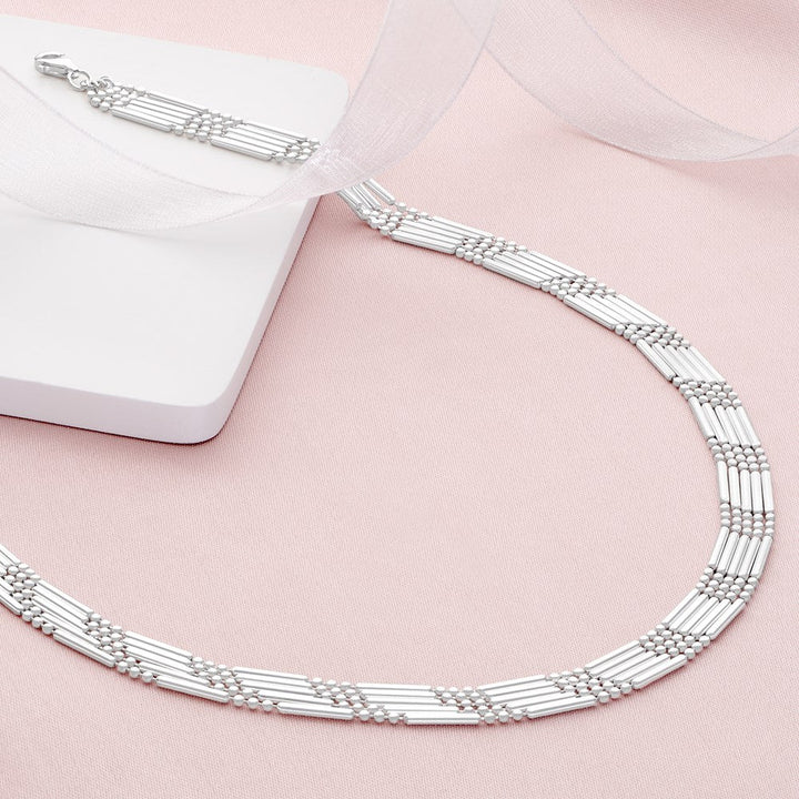 A silver five strand necklace on a pink background.