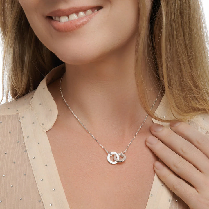 Woman wearing a silver necklace with interlocking rings on a neutral background
