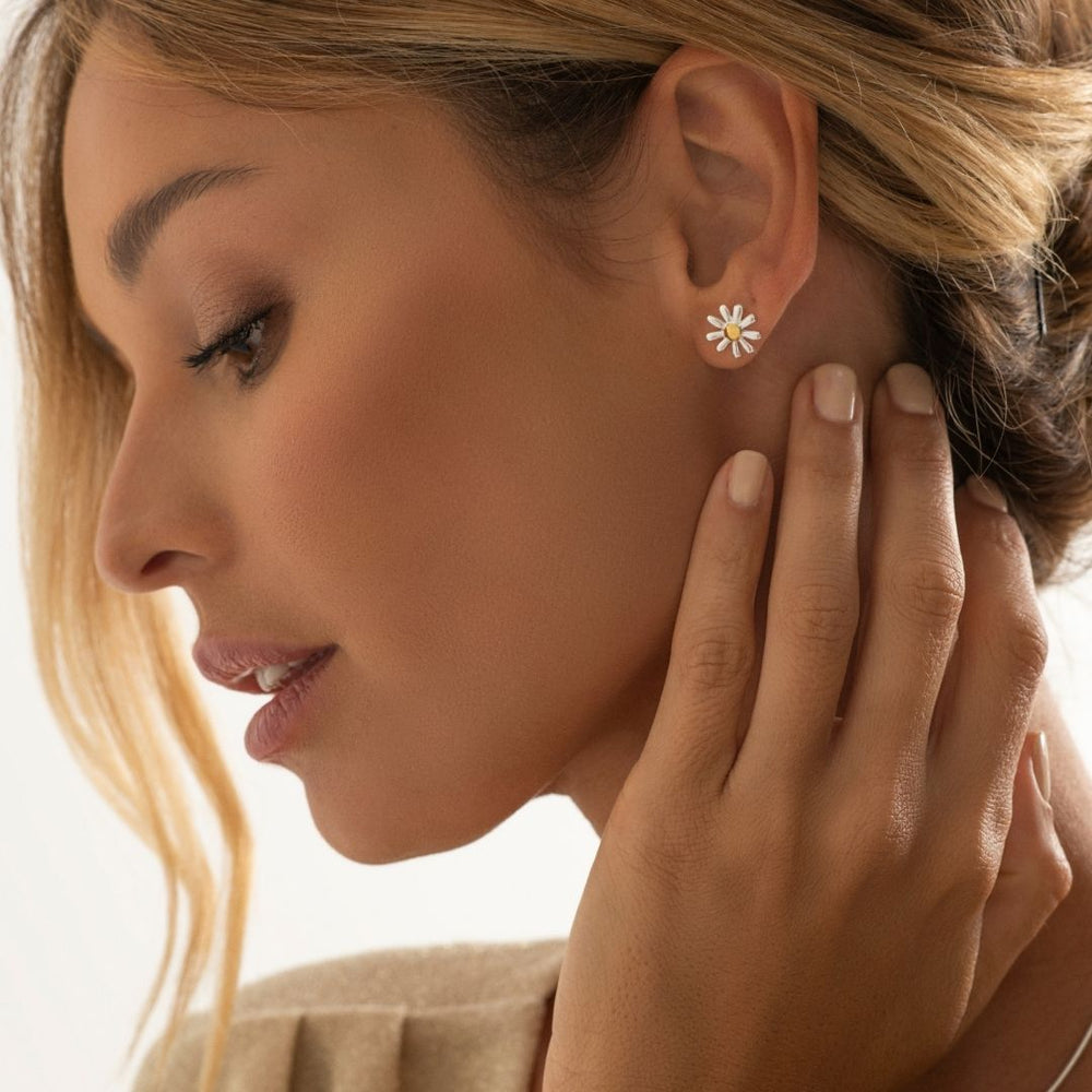 A woman wearing 925 sterling silver daisy stud earrings with a gold-plated center.