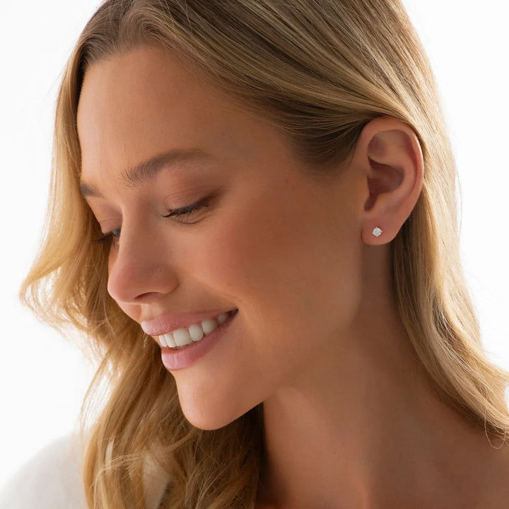 A model wearing a pair of silver stud earrings with solitaire cubic zirconia stones set on a raised platform, giving a diamond-like sparkle.