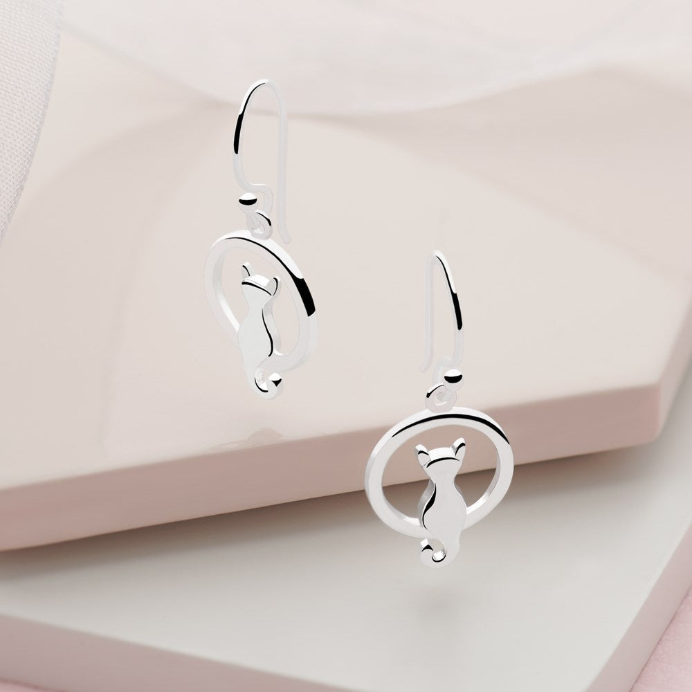 A pair of sterling silver earrings in the design of a cat sitting inside a circle with a tail loop, high polish finish on neutral background. 