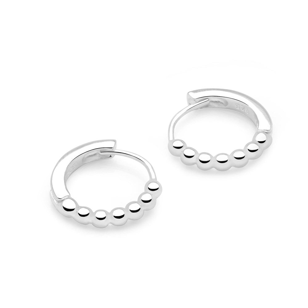 A pair of silver huggie hoop earrings with a beaded design on a white background.