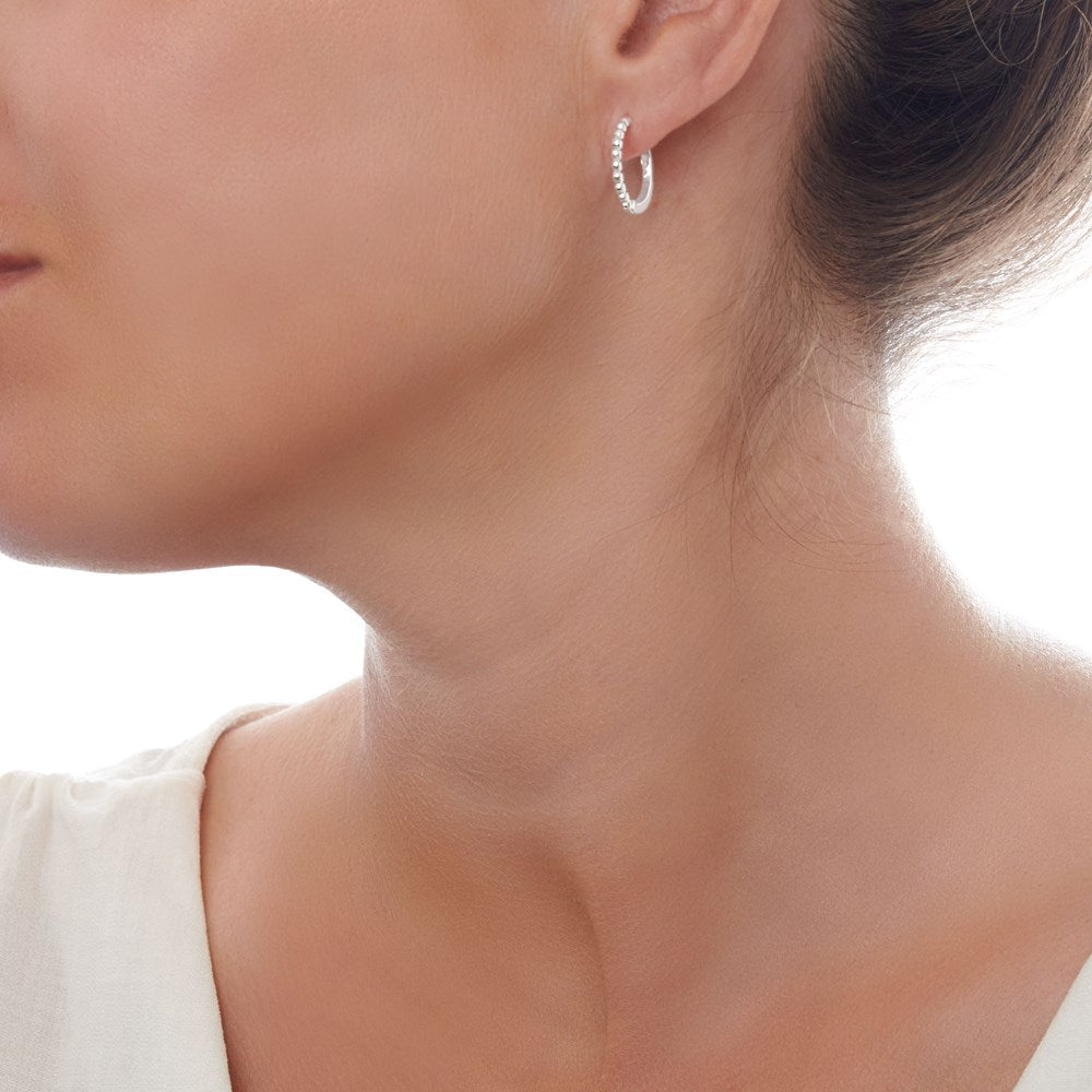A pair of silver huggie hoop earrings with a beaded design on a female model