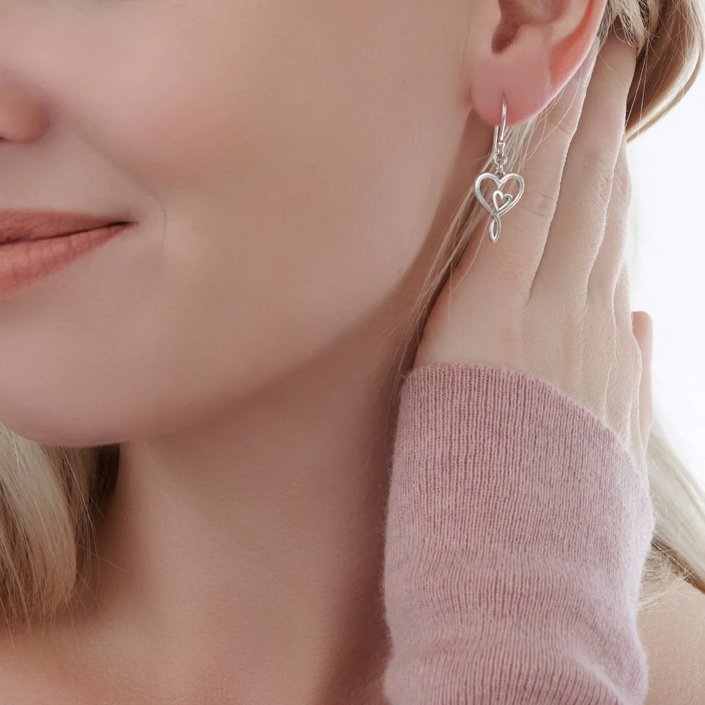 A pair of silver earrings designed with two hearts entwined together on model