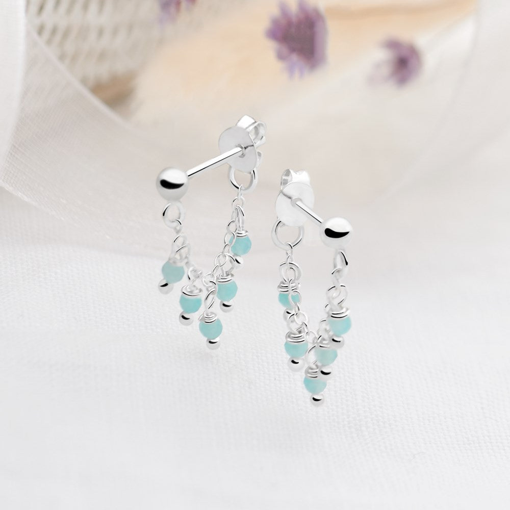 A pair of silver drop earrings with amazonite beads hanging from them, displayed against a neutral background.