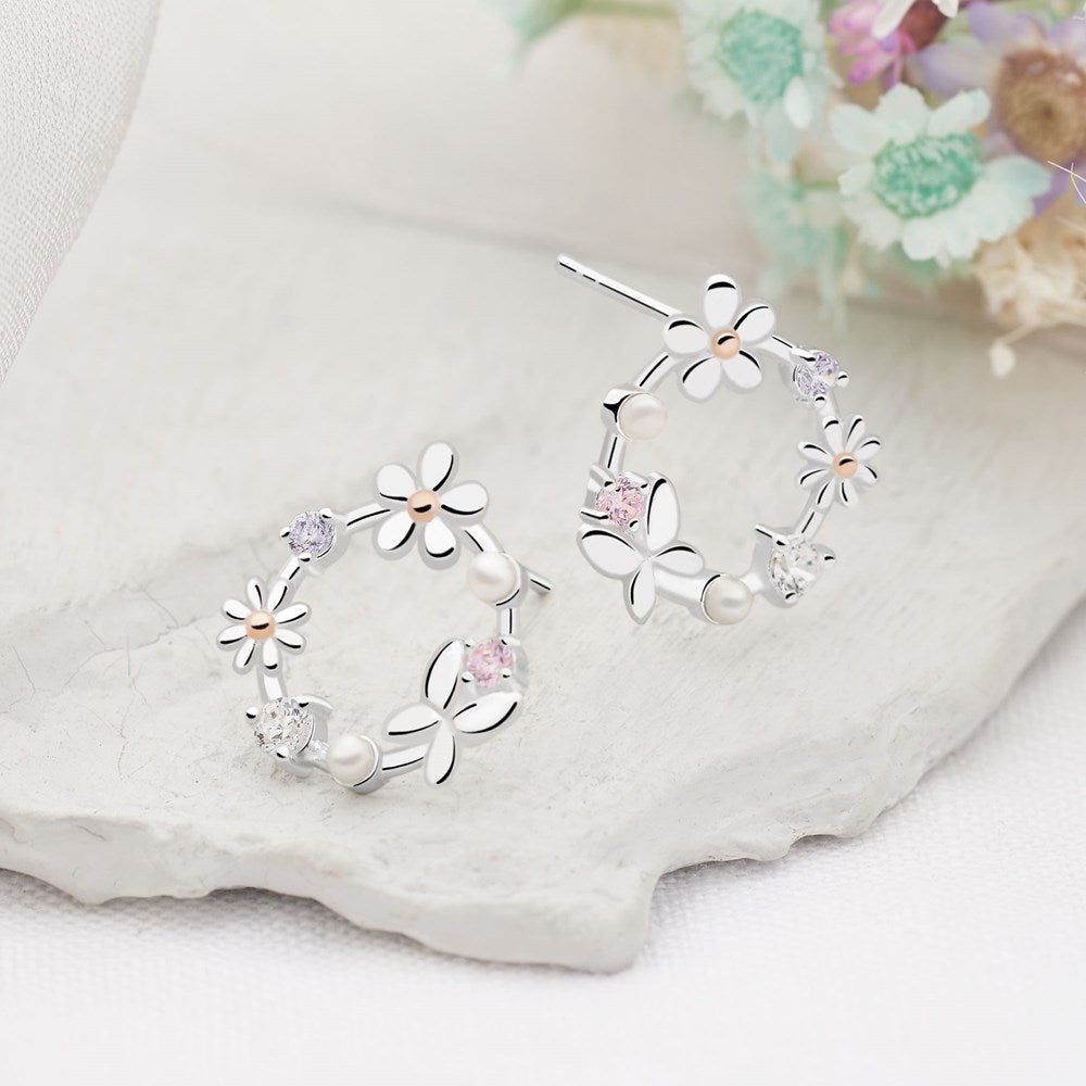 A pair of silver earrings featuring a circle design with butterfly and daisy embellishments, along with pearls and cubic zirconia stones.