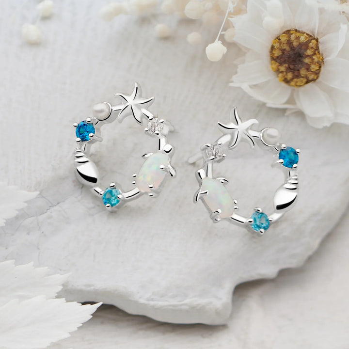 A pair of silver earrings featuring a sea-themed design with opals, pearls, and sparkling cubic zirconia stones arranged in the shape of an ocean reef.