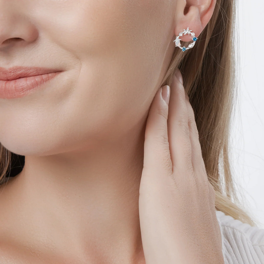 A pair of silver earrings featuring a sea-themed design with opals, pearls, and sparkling cubic zirconia stones arranged in the shape of an ocean reef on model.