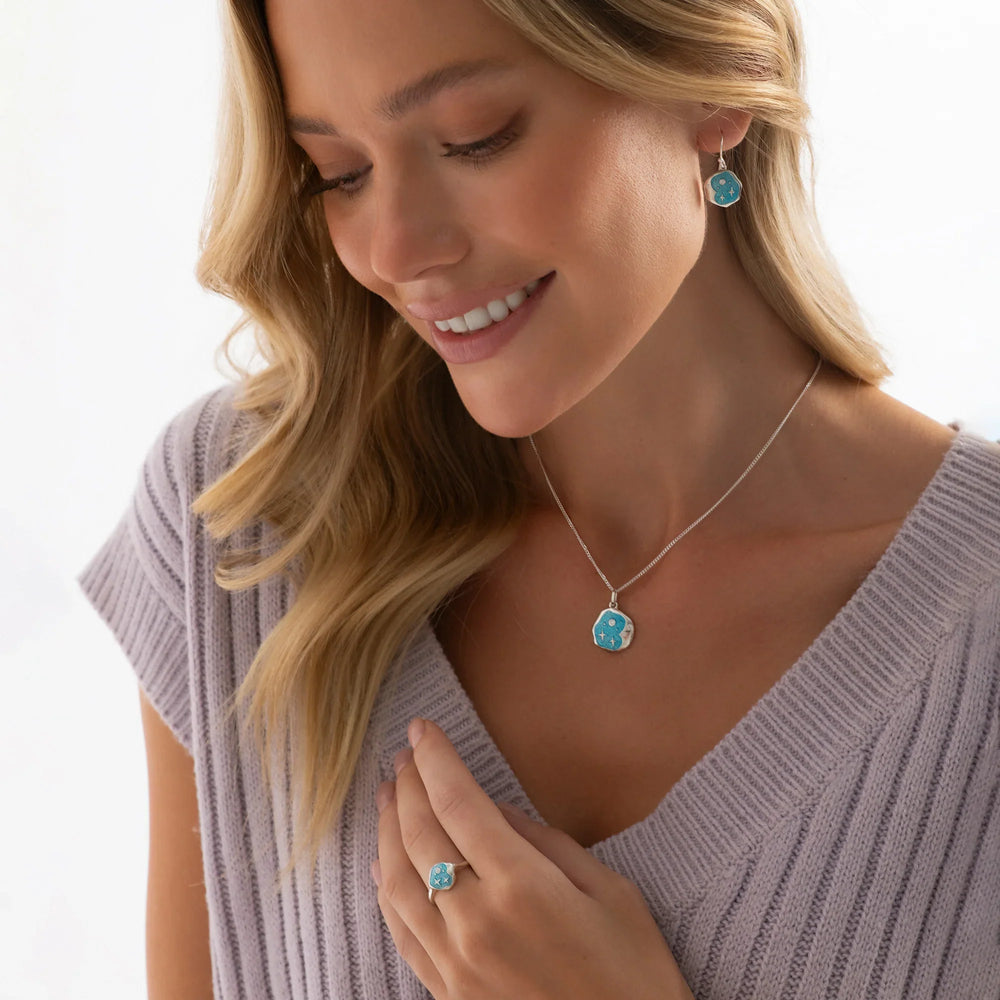 A silver pendant with a crescent moon shape, featuring blue green resin and silver stars, attached to a silver curb chain on woman model. 