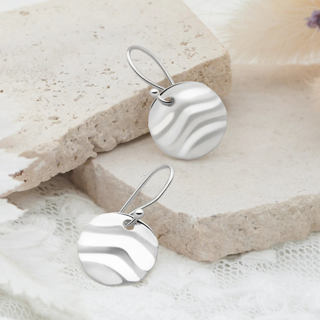 Silver earrings with wavy design on a textured beige surface