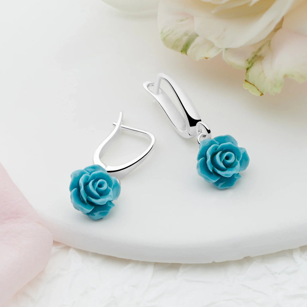 Pair of turquoise rose earrings on a white surface with floral background