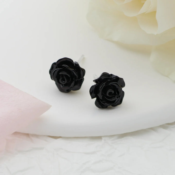 Black rose-shaped earrings on a white fabric background