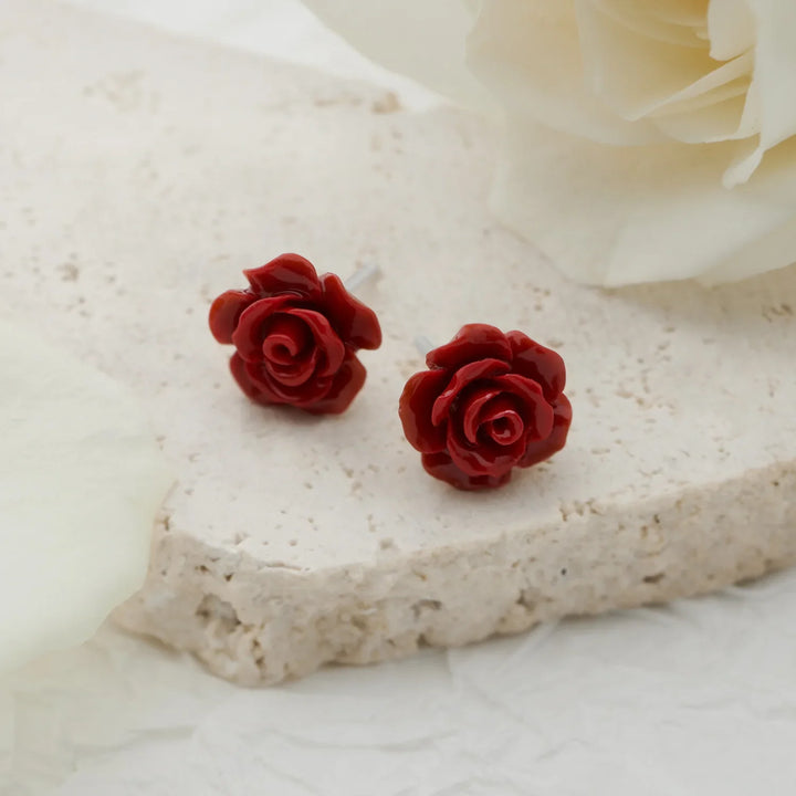 Red rose-shaped earrings on a white stone surface with a white flower in the background.