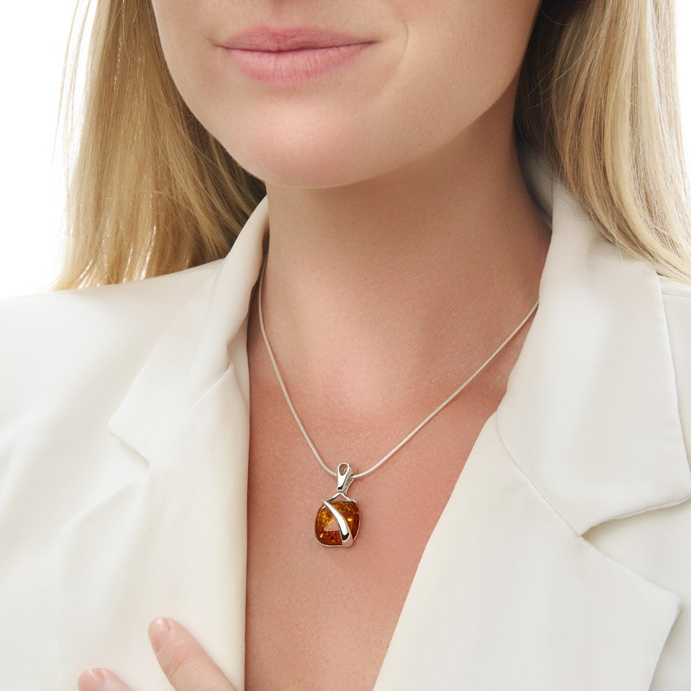 A silver pendant featuring a cushion of amber with a swoosh of silver over it, attached to a 40cm snake chain.