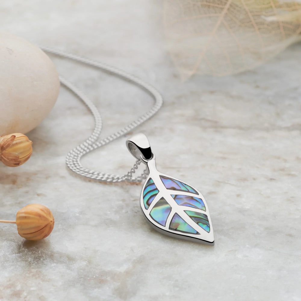 Silver necklace with a leaf-shaped pendant on a light surface