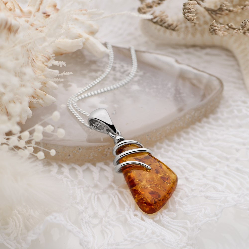 A polished amber pendant wrapped in silver wire on a silver chain against a neutral background.