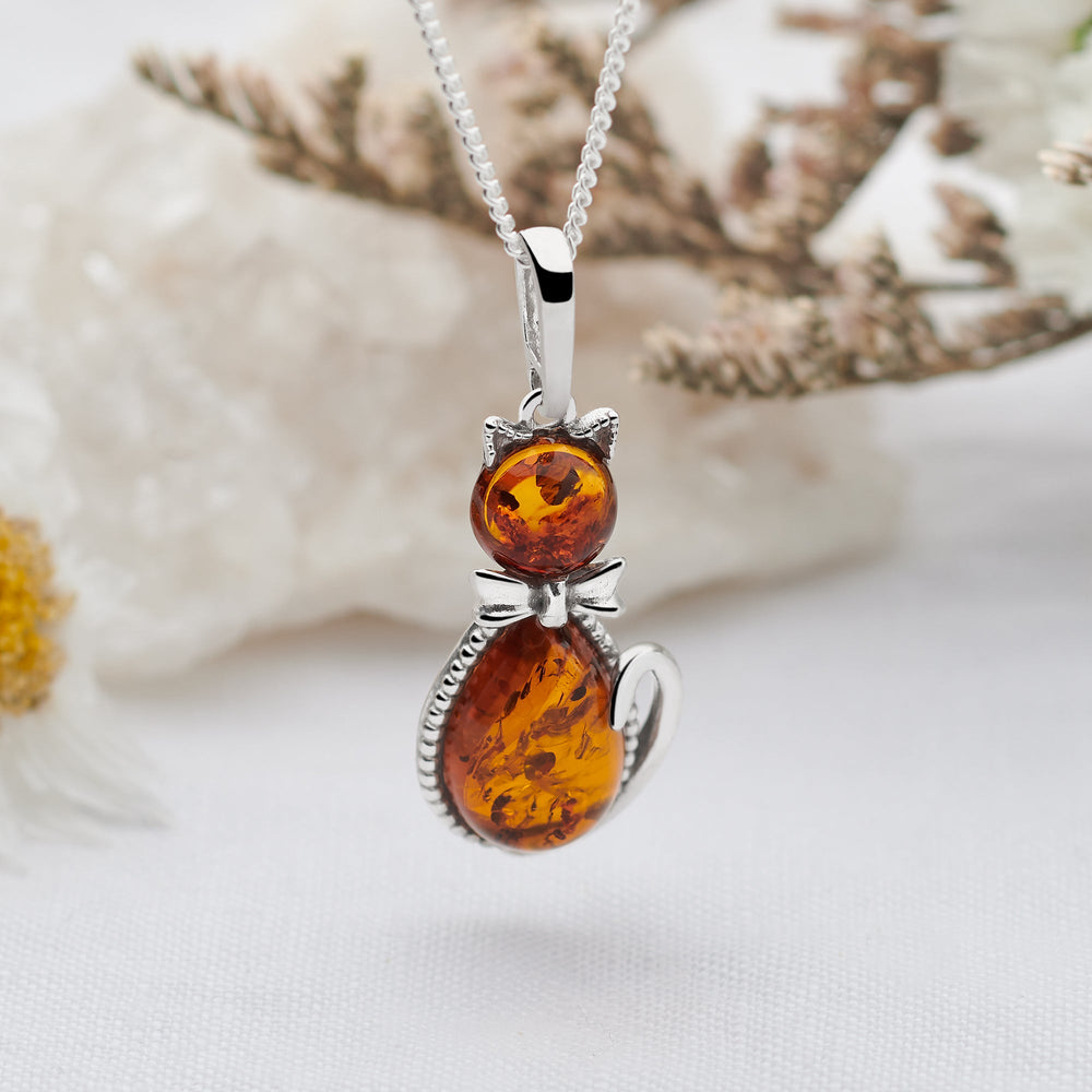 An amber kitten pendant with a silver chain, displayed against a natural stone background.