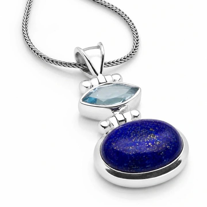 An intricate silver pendant featuring a marquise-cut light blue gemstone set above a larger oval deep blue lapis lazuli stone, suspended from a textured silver chain.