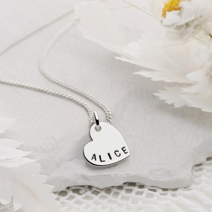 Silver necklace with a heart-shaped pendant engraved with 'ALICE' on a white floral background