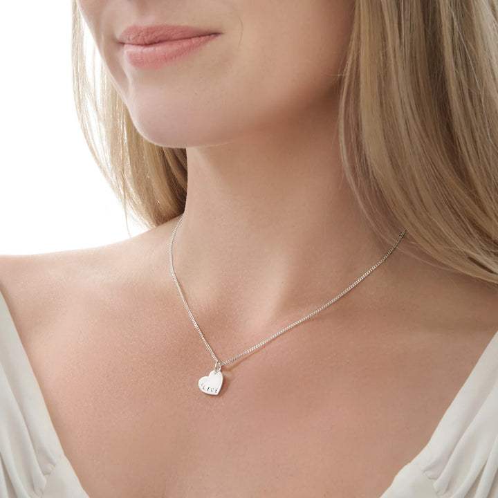 Silver heart-shaped pendant necklace on a model with a plain background
