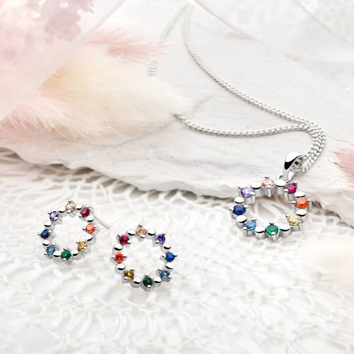 A silver pendant with a halo-like design consisting of multiple colorful cubic zirconia stones arranged in a circle, attached to a silver chain.