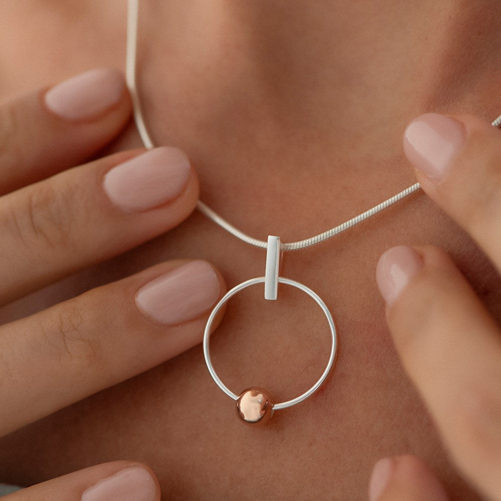 A silver pendant featuring a hoop with a rose gold plated moon inside, attached to a snake chain necklace.