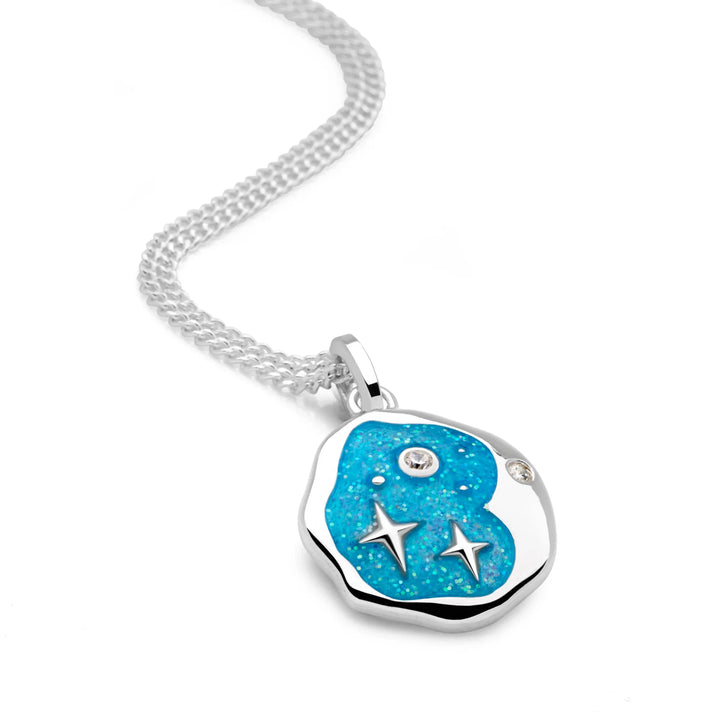 A silver pendant with a crescent moon shape, featuring blue green resin and silver stars, attached to a silver curb chain.