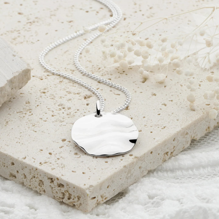 Silver necklace with a heart-shaped pendant on a textured stone surface