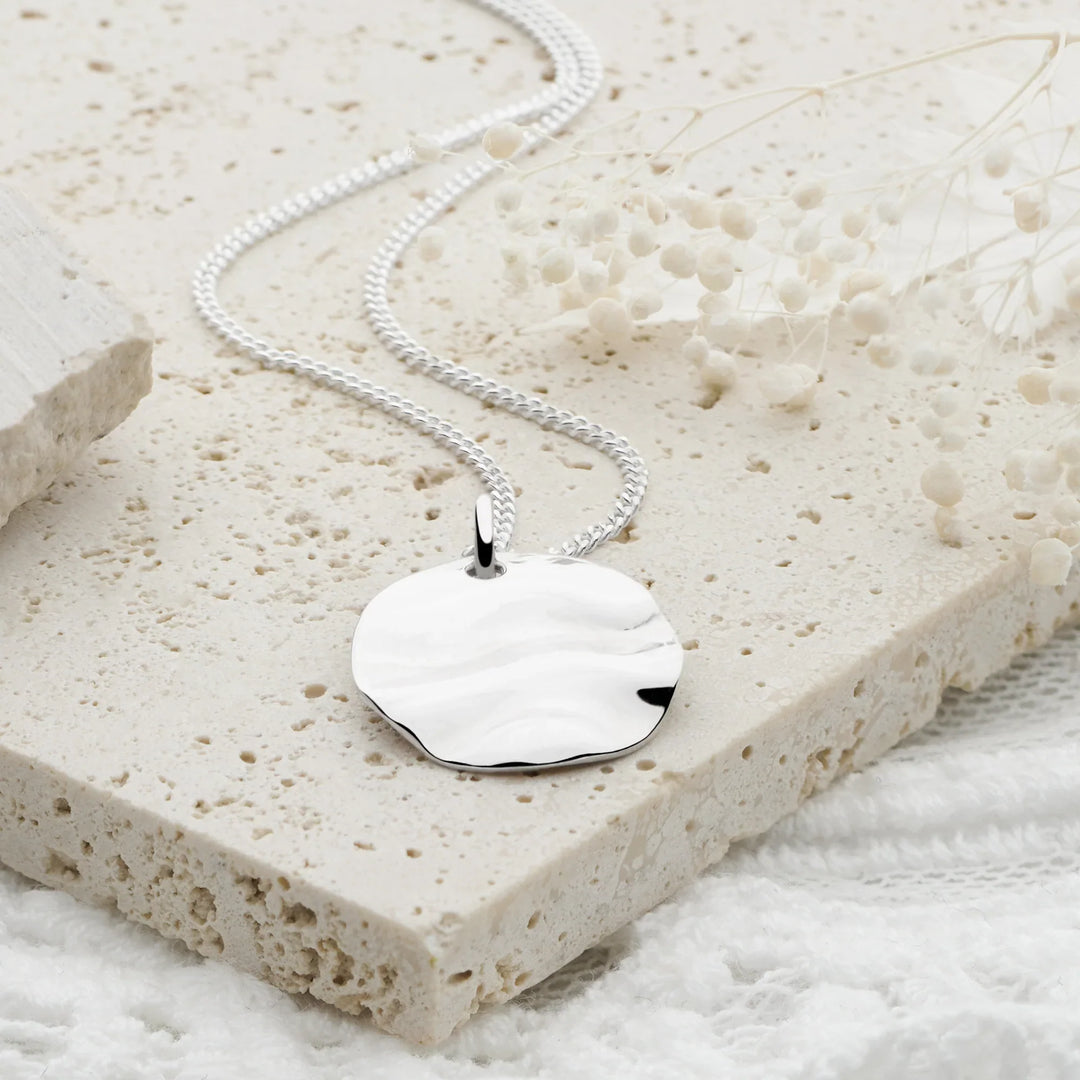 Silver necklace with a heart-shaped pendant on a textured stone surface