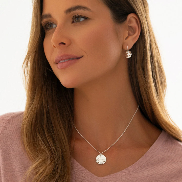 Woman wearing a silver necklace and earrings on a plain background
