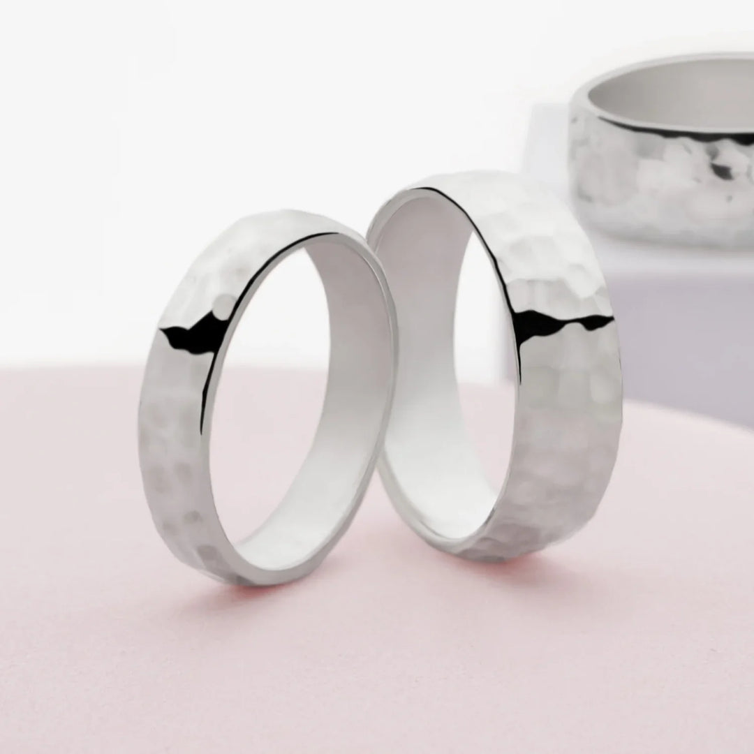A silver band ring with a hammered finish, displayed on a neutral background.