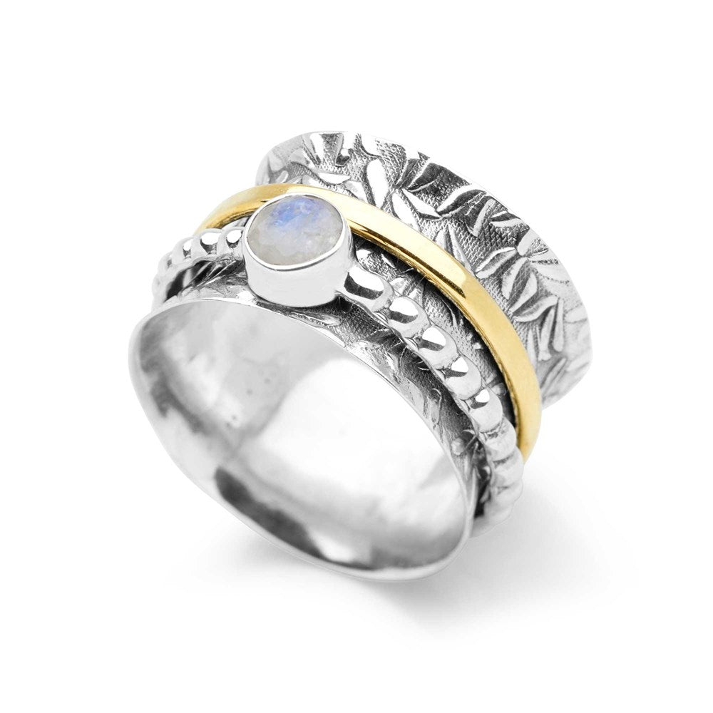 A silver ring with a leafy forest frieze design, featuring a golden brass band and a spinning moonstone.