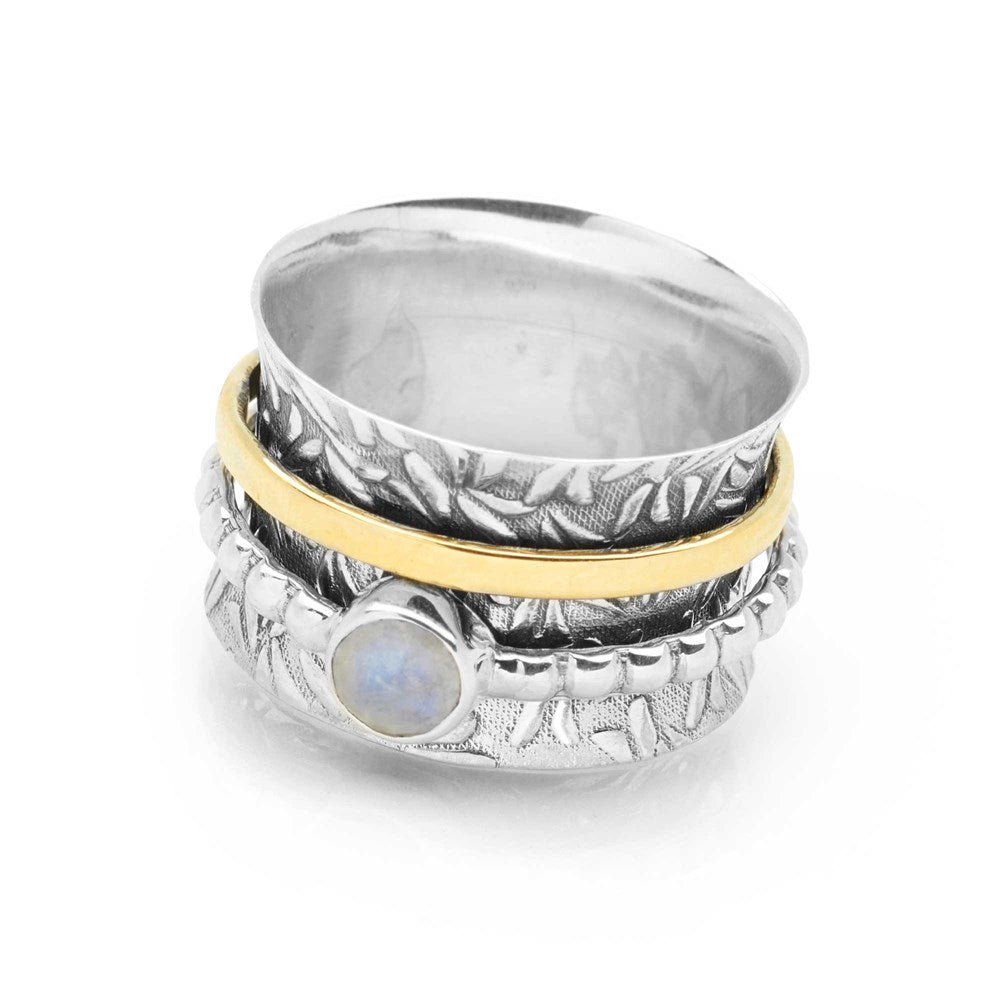 A silver ring with a leafy forest frieze design, featuring a golden brass band and a spinning moonstone.
